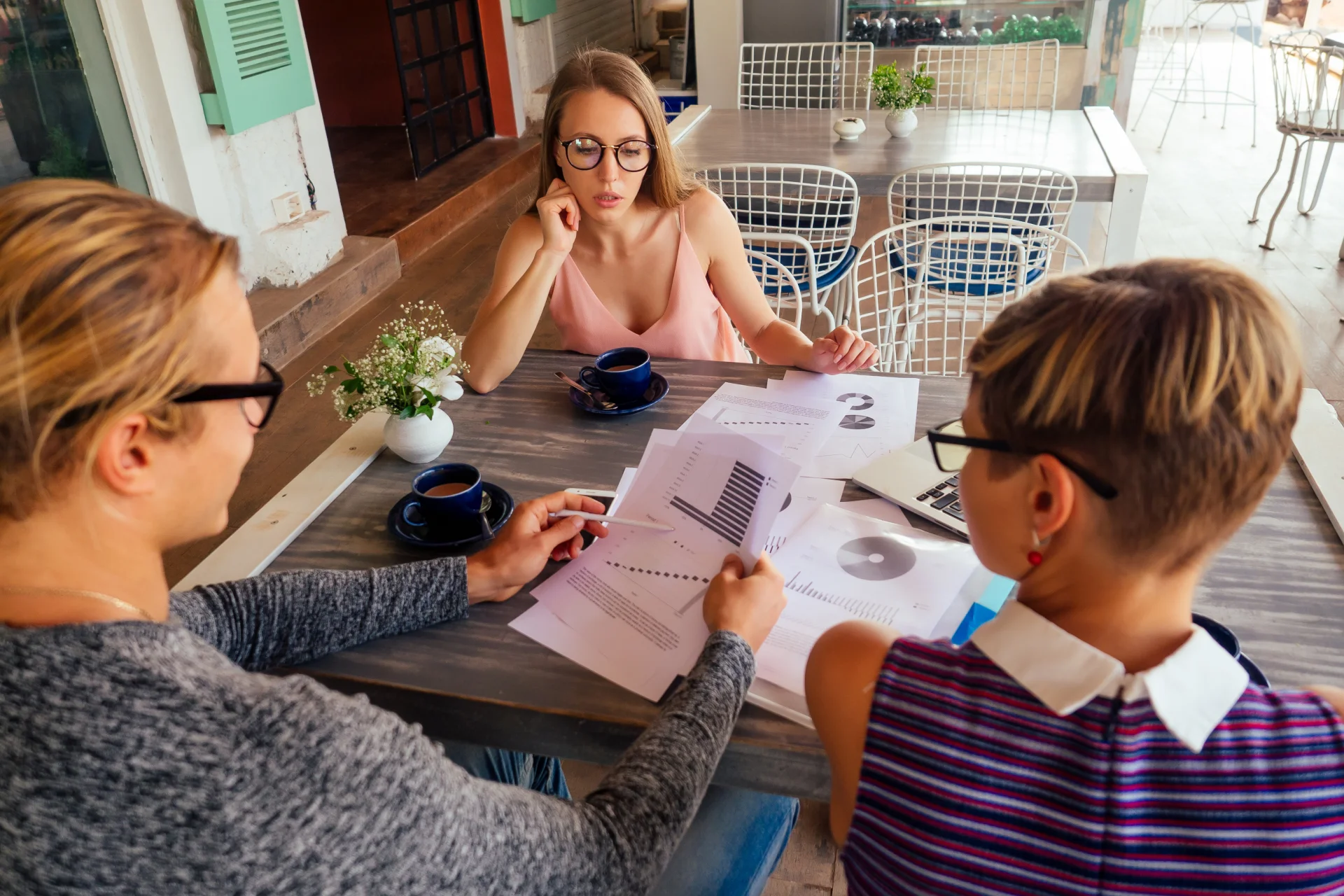 People gathered around a table discussing intervention strategies, reviewing printed materials, and drinking coffee in a supportive environment.